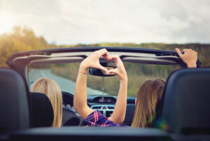 Two girls in convertable making heart with their hands